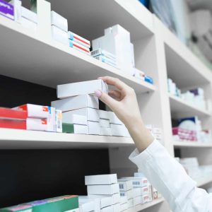 Closeup view of pharmacist hand taking medicine box from the shelf in drug store.